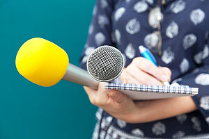 Hand holding two microphones, a notepad and a pen