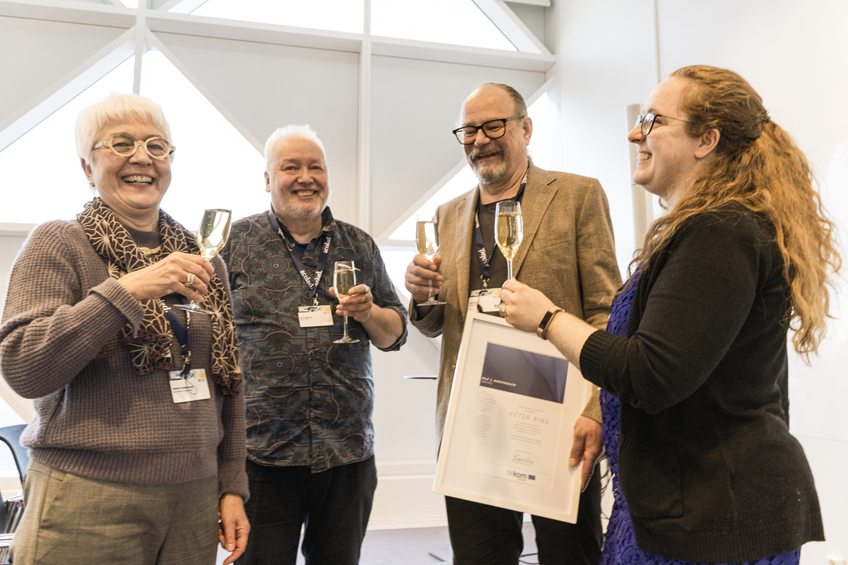 award winner Peter Ring standing between the committee members holding his certificate and all toasting with a glass of sparkling wine
